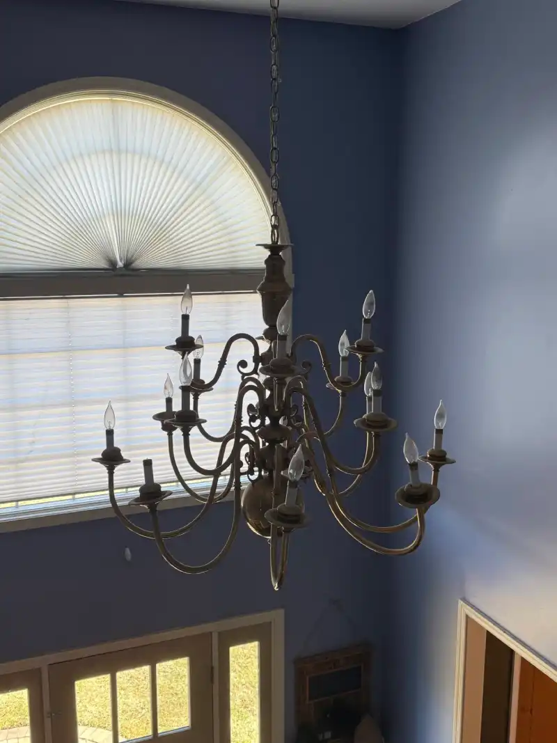 A professional electrician installing a large multi-tier brass chandelier